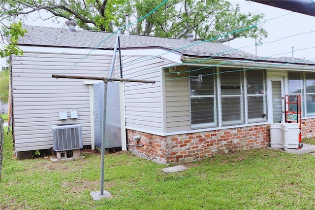 view of side of property with brick siding, a shingled roof, central AC, and a yard