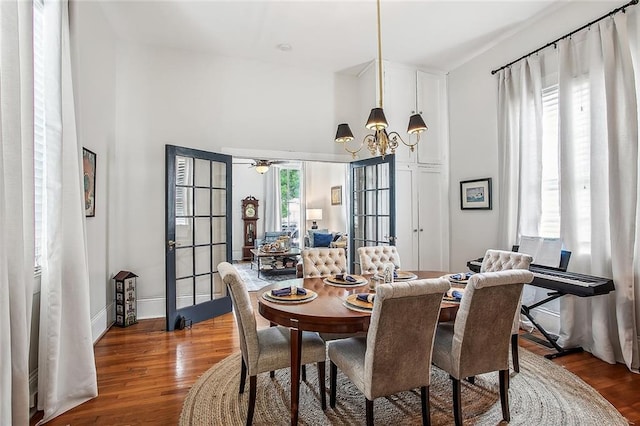 dining space with french doors, wood finished floors, baseboards, a towering ceiling, and an inviting chandelier