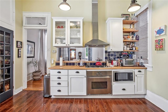 kitchen with open shelves, dark wood-style flooring, stainless steel appliances, wall chimney range hood, and white cabinets