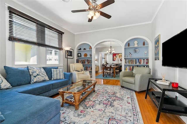 living area with ornamental molding, built in shelves, wood finished floors, and ceiling fan with notable chandelier