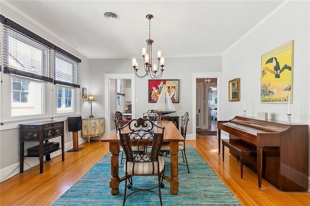 dining room with light wood finished floors, a notable chandelier, visible vents, and crown molding