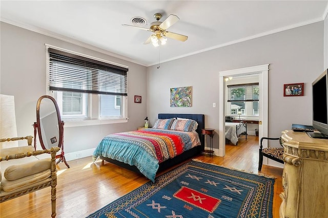 bedroom with crown molding, a ceiling fan, visible vents, wood finished floors, and baseboards