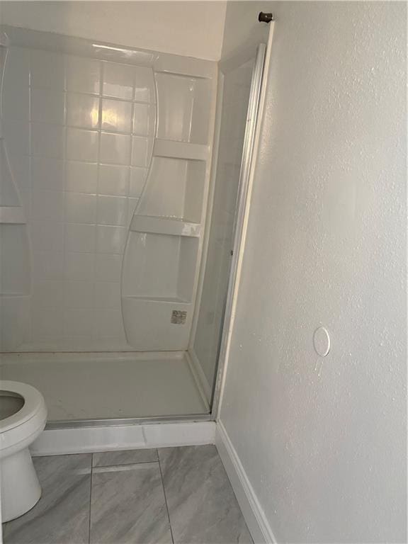 bathroom featuring a shower stall, baseboards, toilet, and a textured wall