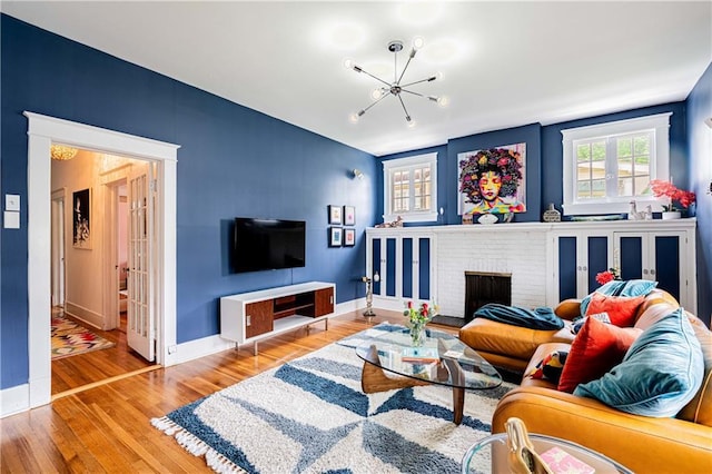 living area with wood finished floors, an inviting chandelier, baseboards, and a fireplace