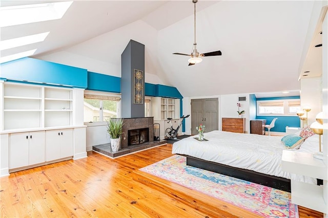 bedroom with wood-type flooring, a skylight, multiple windows, and a fireplace
