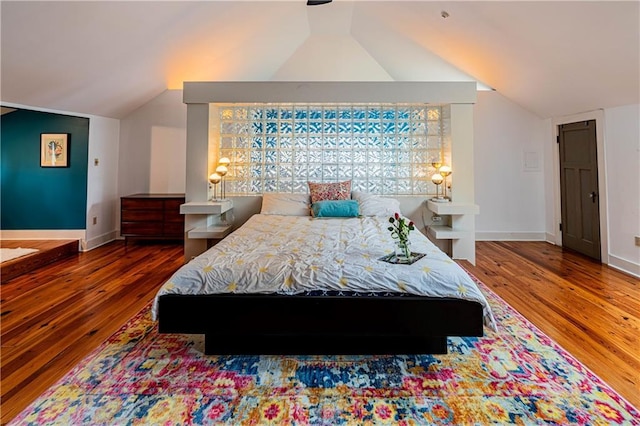 bedroom featuring baseboards, wood finished floors, and lofted ceiling