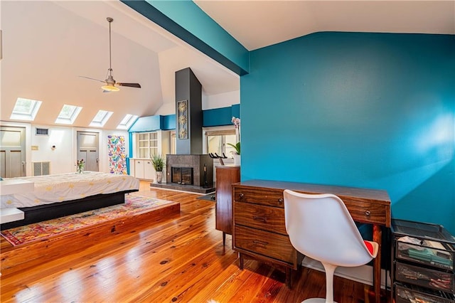 bedroom with vaulted ceiling with skylight, wood finished floors, and a glass covered fireplace