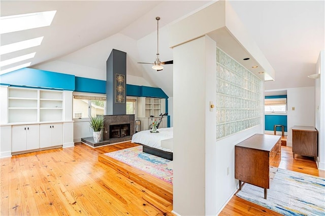 living room with wood-type flooring, vaulted ceiling with skylight, a multi sided fireplace, and a healthy amount of sunlight
