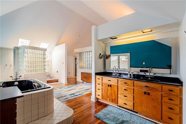 kitchen featuring vaulted ceiling with skylight, backsplash, brown cabinetry, a sink, and wood finished floors