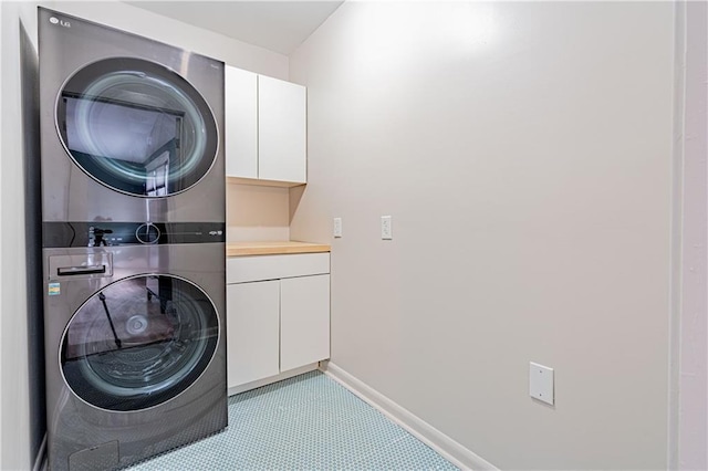 clothes washing area with stacked washer and dryer, baseboards, and cabinet space