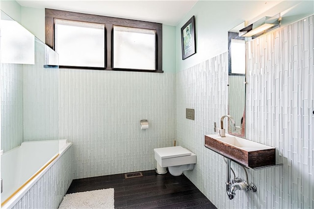 full bath featuring toilet, visible vents, tile walls, a sink, and wood finished floors