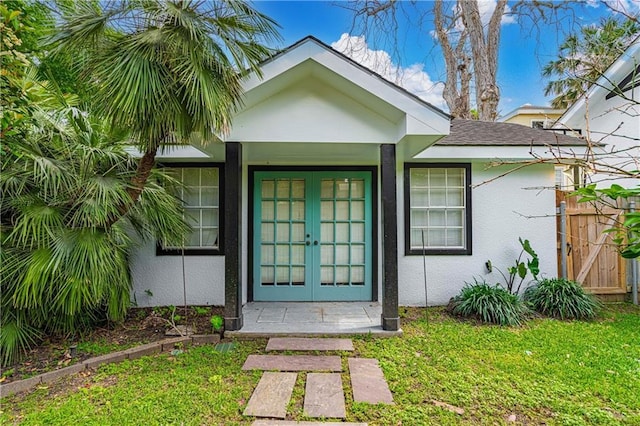 entrance to property featuring a yard, french doors, and stucco siding