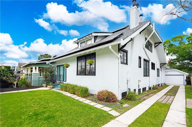 view of front facade featuring stucco siding, an outdoor structure, a chimney, a front yard, and solar panels