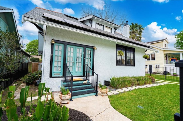 view of front of house with stucco siding, entry steps, a front yard, fence, and solar panels