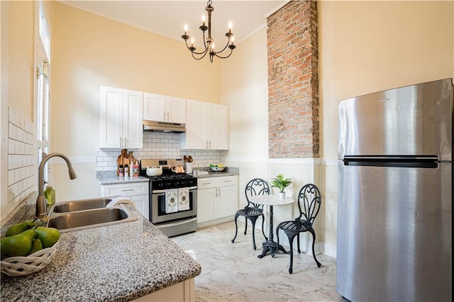 kitchen with a towering ceiling, white cabinetry, under cabinet range hood, appliances with stainless steel finishes, and a sink
