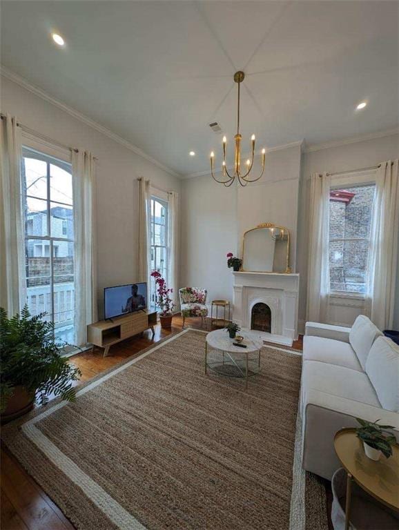 living room featuring an inviting chandelier, a fireplace, crown molding, recessed lighting, and wood finished floors