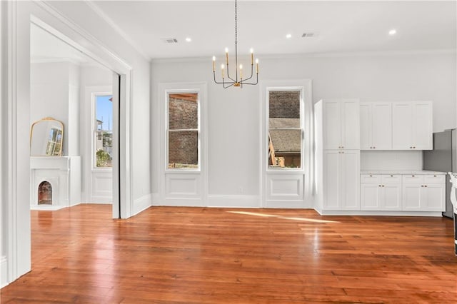 unfurnished dining area featuring ornamental molding, a chandelier, visible vents, and hardwood / wood-style flooring