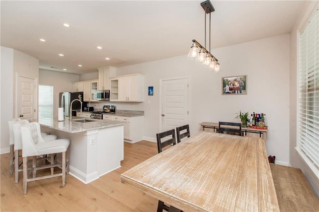 201 Belle Pointe Dr, Madisonville, LA 70447 - kitchen featuring stainless steel appliances, a kitchen island with sink, white cabinets, light wood-type flooring, and a kitchen breakfast bar
