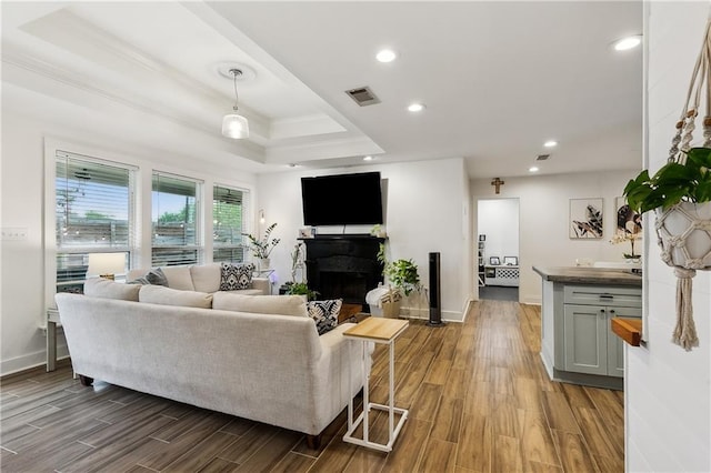 living room featuring visible vents, baseboards, a raised ceiling, ornamental molding, and wood finished floors