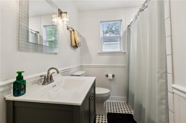 bathroom with toilet, vanity, a shower with curtain, and a wainscoted wall