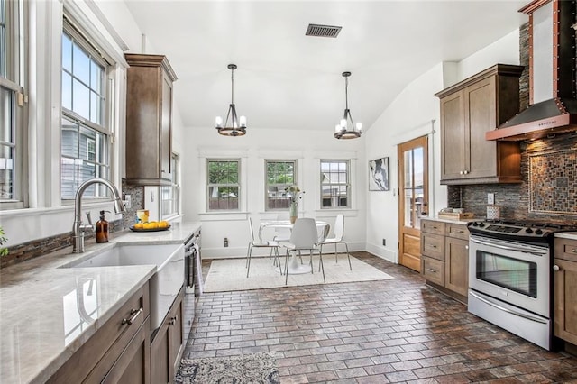 kitchen with wall chimney exhaust hood, tasteful backsplash, stainless steel electric range oven, brick floor, and a notable chandelier