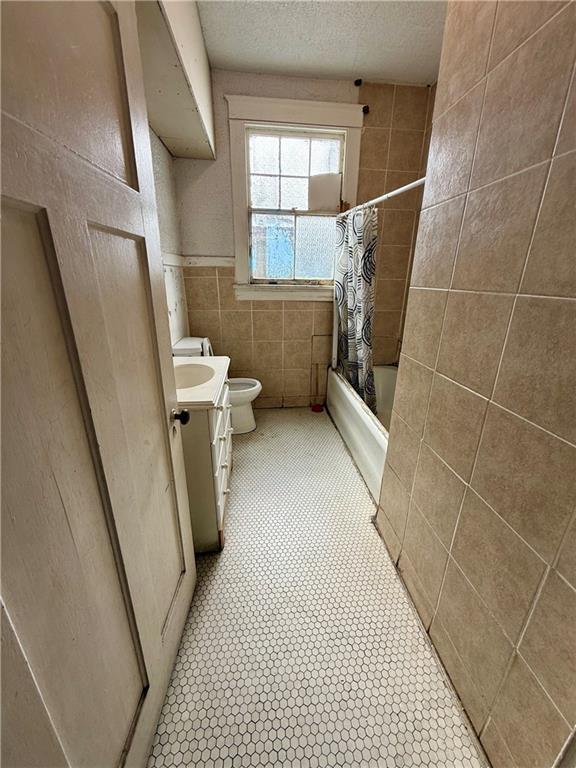 351517 Tulane Ave, New Orleans, LA 70119 - bathroom with a textured ceiling, vanity, toilet, shower / bath combo, and tile walls