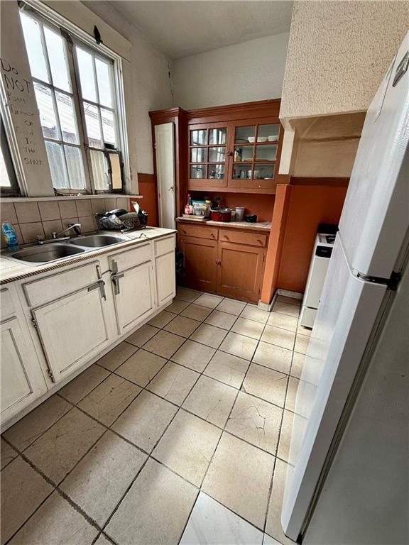 351517 Tulane Ave, New Orleans, LA 70119 - kitchen featuring freestanding refrigerator, glass insert cabinets, stove, a sink, and brown cabinets