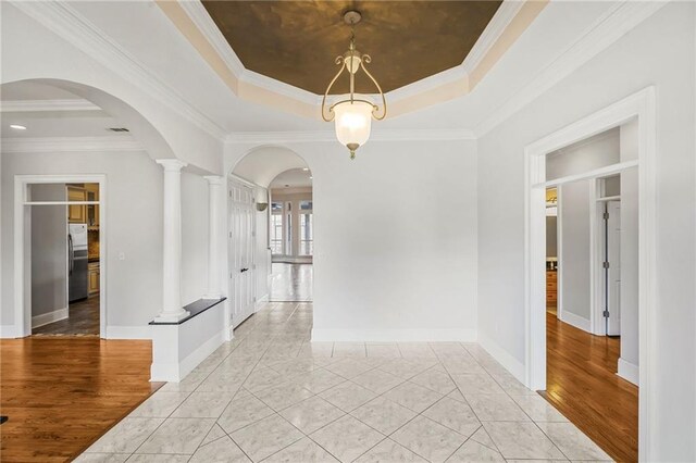 spare room with a raised ceiling, arched walkways, baseboards, crown molding, and decorative columns