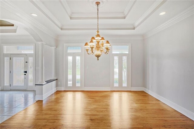 foyer entrance with a tray ceiling, light wood-style floors, a chandelier, and baseboards