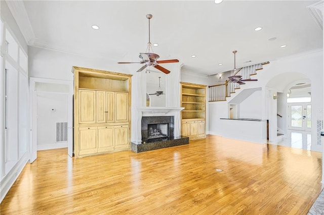 unfurnished living room featuring ceiling fan, ornamental molding, light wood finished floors, stairway, and recessed lighting