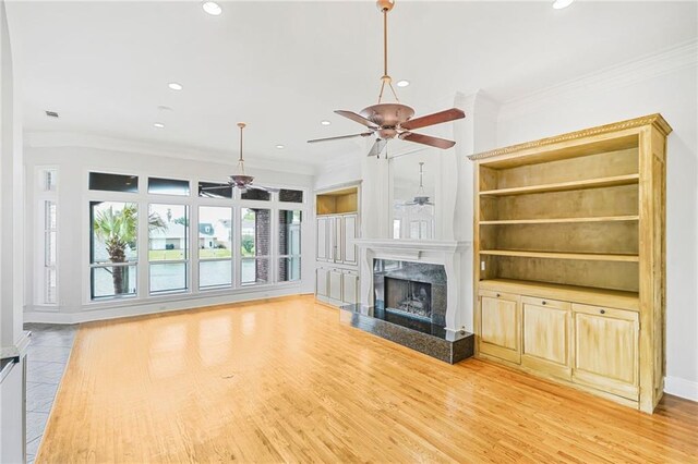unfurnished living room with ceiling fan, a premium fireplace, crown molding, recessed lighting, and light wood-style flooring