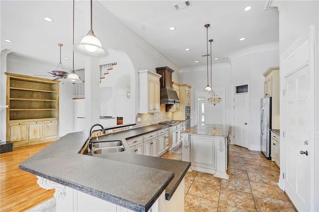 kitchen with a sink, stainless steel appliances, wall chimney range hood, a kitchen island, and cream cabinets