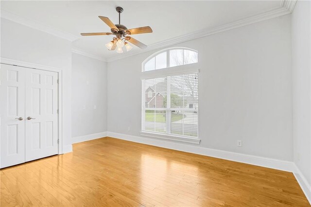 unfurnished bedroom with light wood finished floors, crown molding, baseboards, a closet, and a ceiling fan