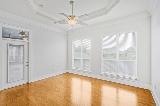 empty room featuring a ceiling fan, a tray ceiling, light wood-style flooring, ornamental molding, and baseboards