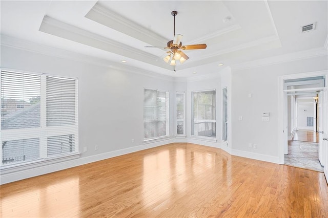 empty room featuring a ceiling fan, a tray ceiling, light wood-style flooring, ornamental molding, and baseboards