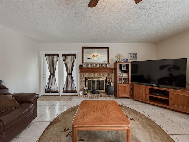 living area with light tile patterned floors, a ceiling fan, a brick fireplace, and a textured ceiling