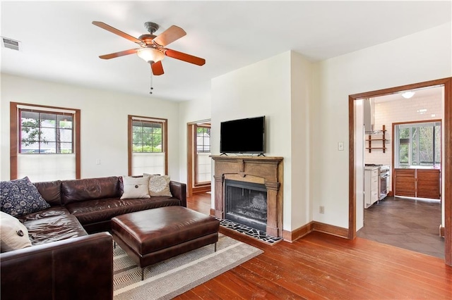 living room with a ceiling fan, baseboards, a fireplace with flush hearth, visible vents, and dark wood-style floors