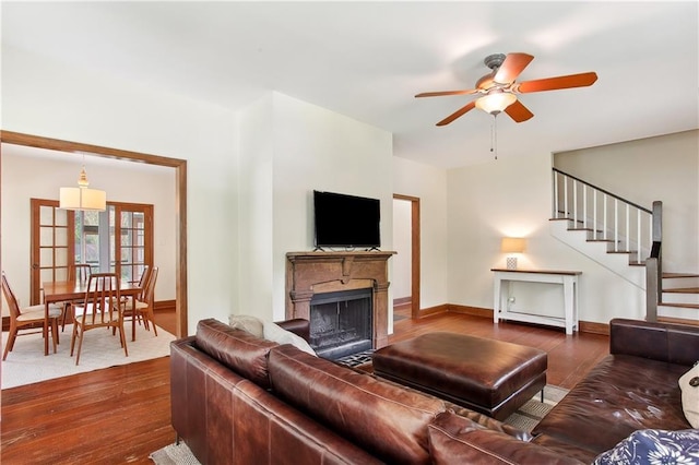 living room featuring ceiling fan, a fireplace, stairway, baseboards, and dark wood-style floors