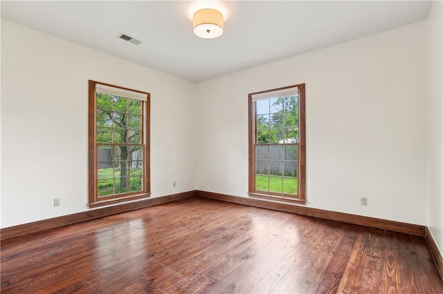 empty room featuring wood-type flooring, baseboards, visible vents, and plenty of natural light