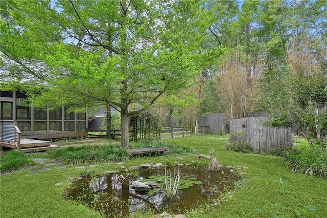 view of yard featuring a small pond, fence, and a sunroom