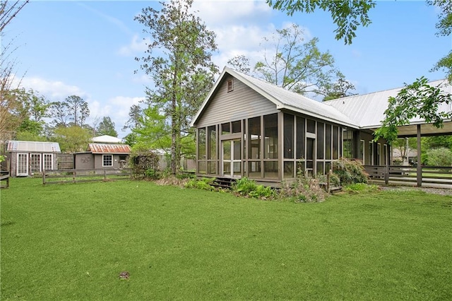 back of house featuring a lawn, an outbuilding, a sunroom, a carport, and fence