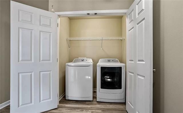 clothes washing area featuring baseboards, independent washer and dryer, laundry area, and wood finished floors