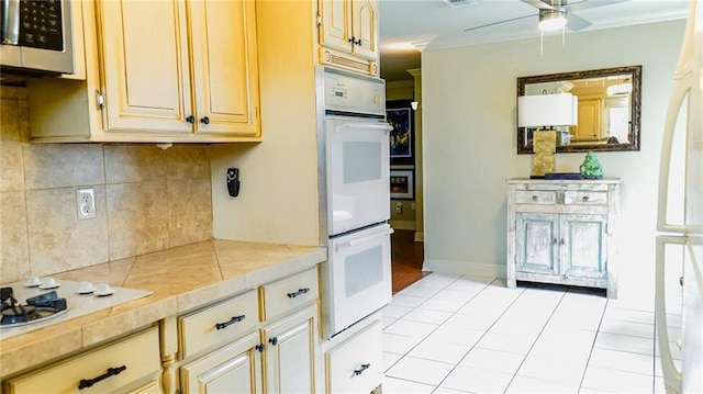 kitchen featuring stainless steel microwave, tasteful backsplash, baseboards, white double oven, and ceiling fan