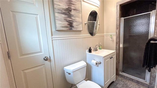 bathroom with a shower stall, toilet, vanity, and a wainscoted wall