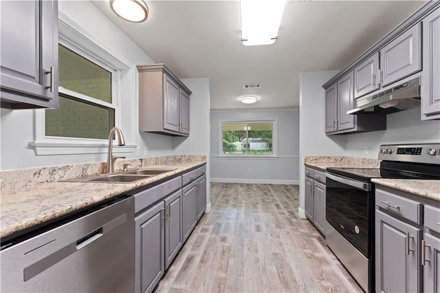 kitchen featuring light wood-type flooring, gray cabinets, under cabinet range hood, a sink, and appliances with stainless steel finishes