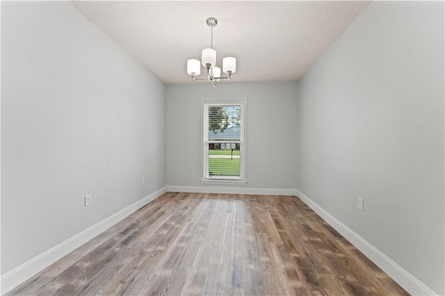 unfurnished room featuring a textured ceiling, baseboards, a chandelier, and wood finished floors