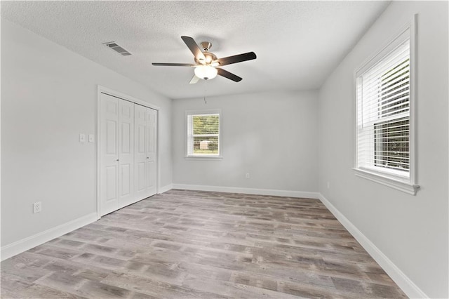 unfurnished bedroom with a textured ceiling, baseboards, wood finished floors, visible vents, and a closet