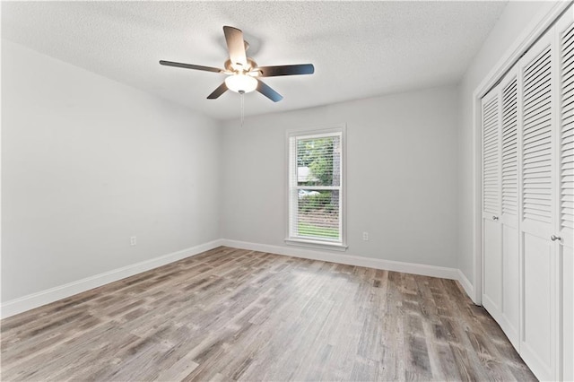 unfurnished bedroom with a closet, wood finished floors, baseboards, a textured ceiling, and a ceiling fan