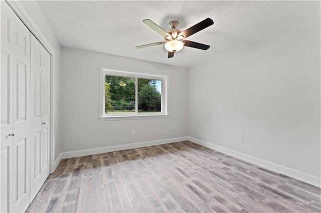 unfurnished bedroom with a textured ceiling, baseboards, light wood-style floors, and a closet