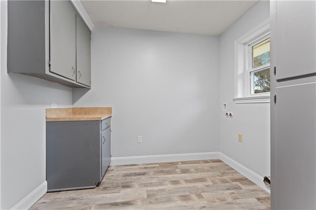 laundry room with baseboards, a textured ceiling, light wood-style flooring, and cabinet space